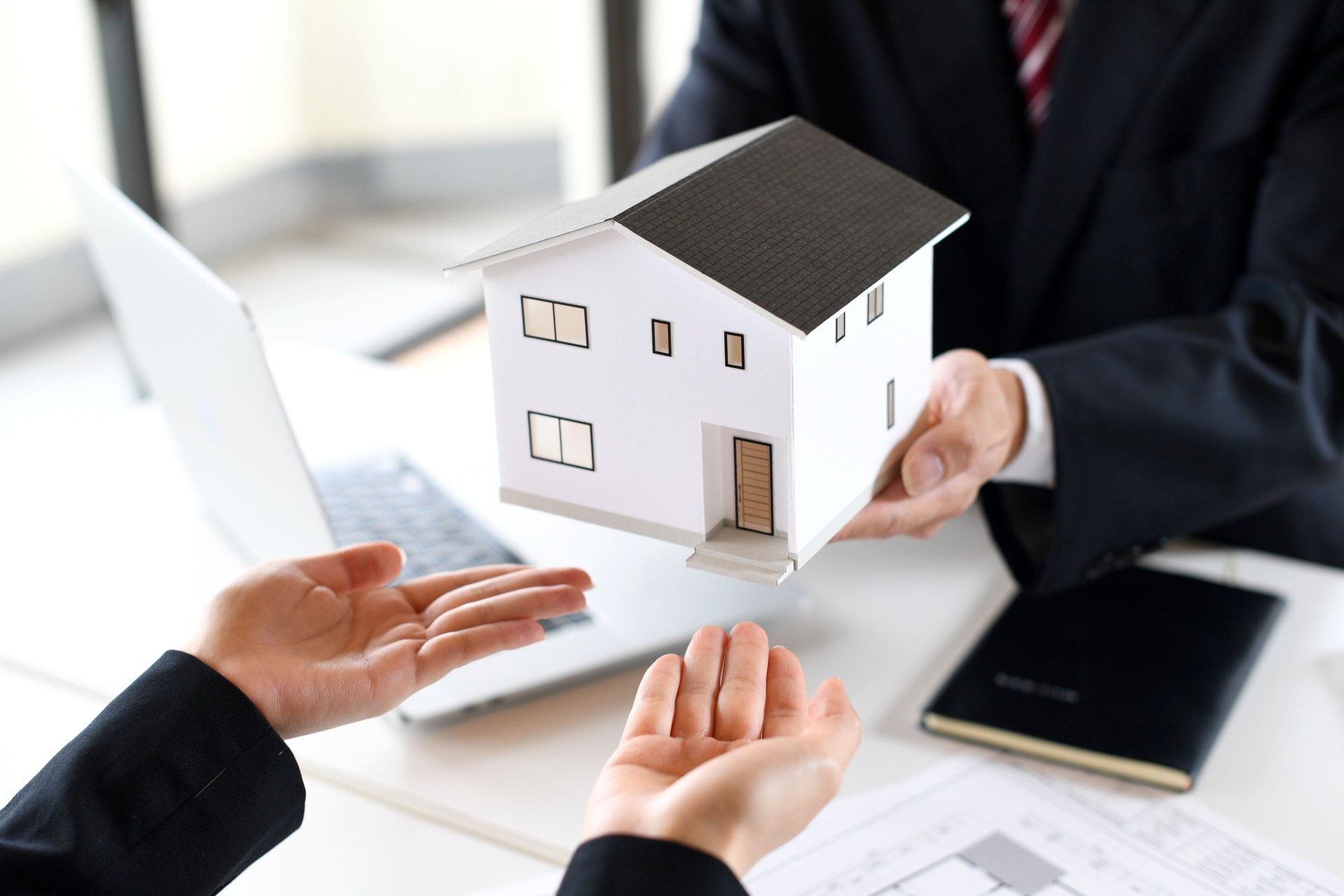 A male office worker in a suit hands a female office worker an architectural model of real estate.